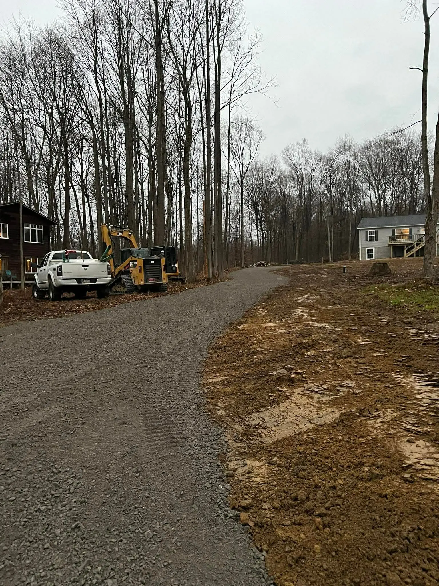 Skid steer and pickup parked at a freshly cut driveway in winter